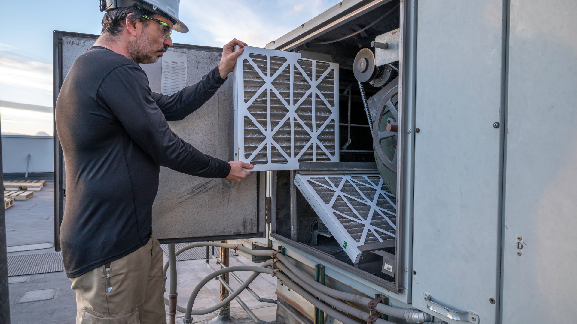 HVAC technician performing preventive maintenance by changing filters on a rooftop unit