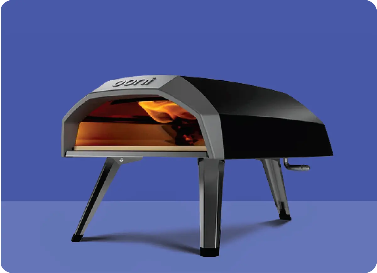 Portable black and gray outdoor pizza oven with fire visible inside, standing on four legs against a blue background.