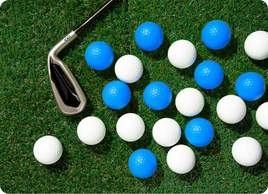Golf club resting on green grass next to scattered white and blue golf balls.