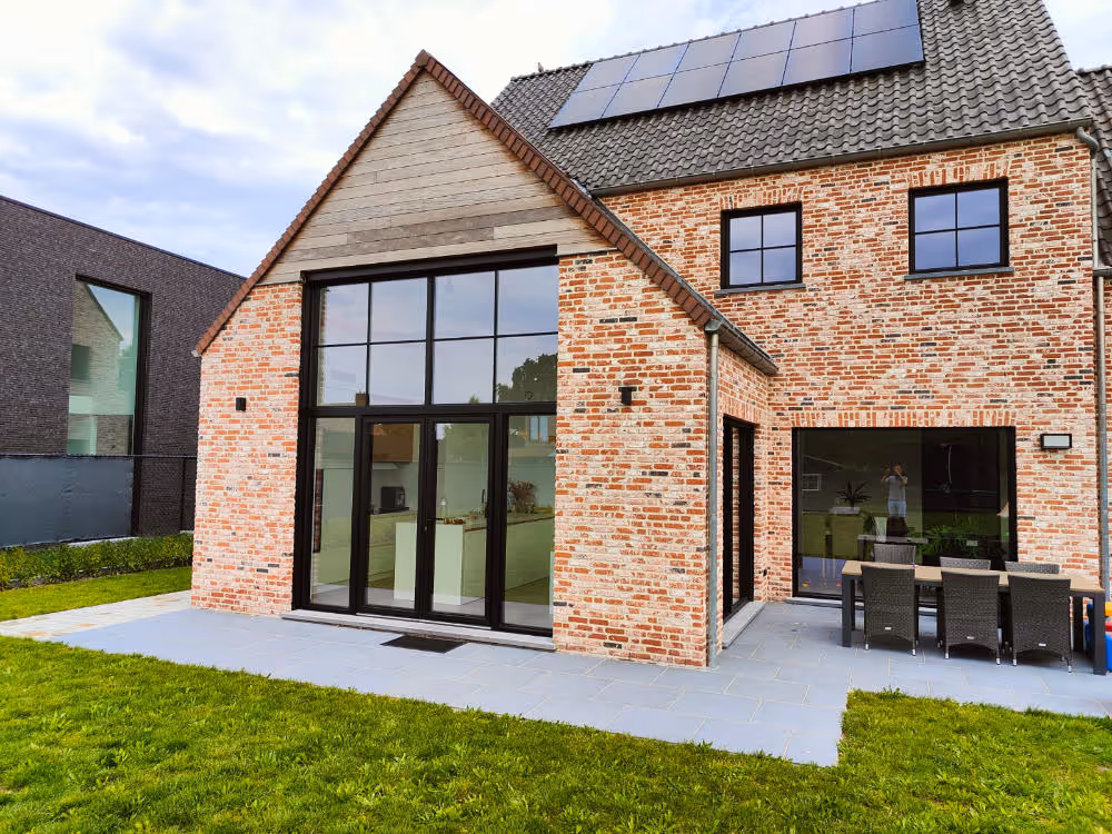 Moderne villa met grote zwarte aluminium ramen en schuifdeuren in landelijke bakstenen gevel