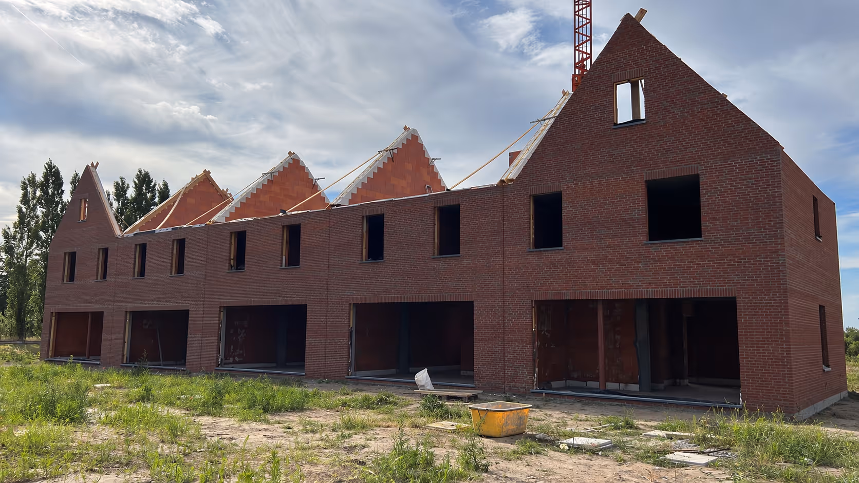 Row of brick townhouses under construction with partially completed roofs and open window frames.