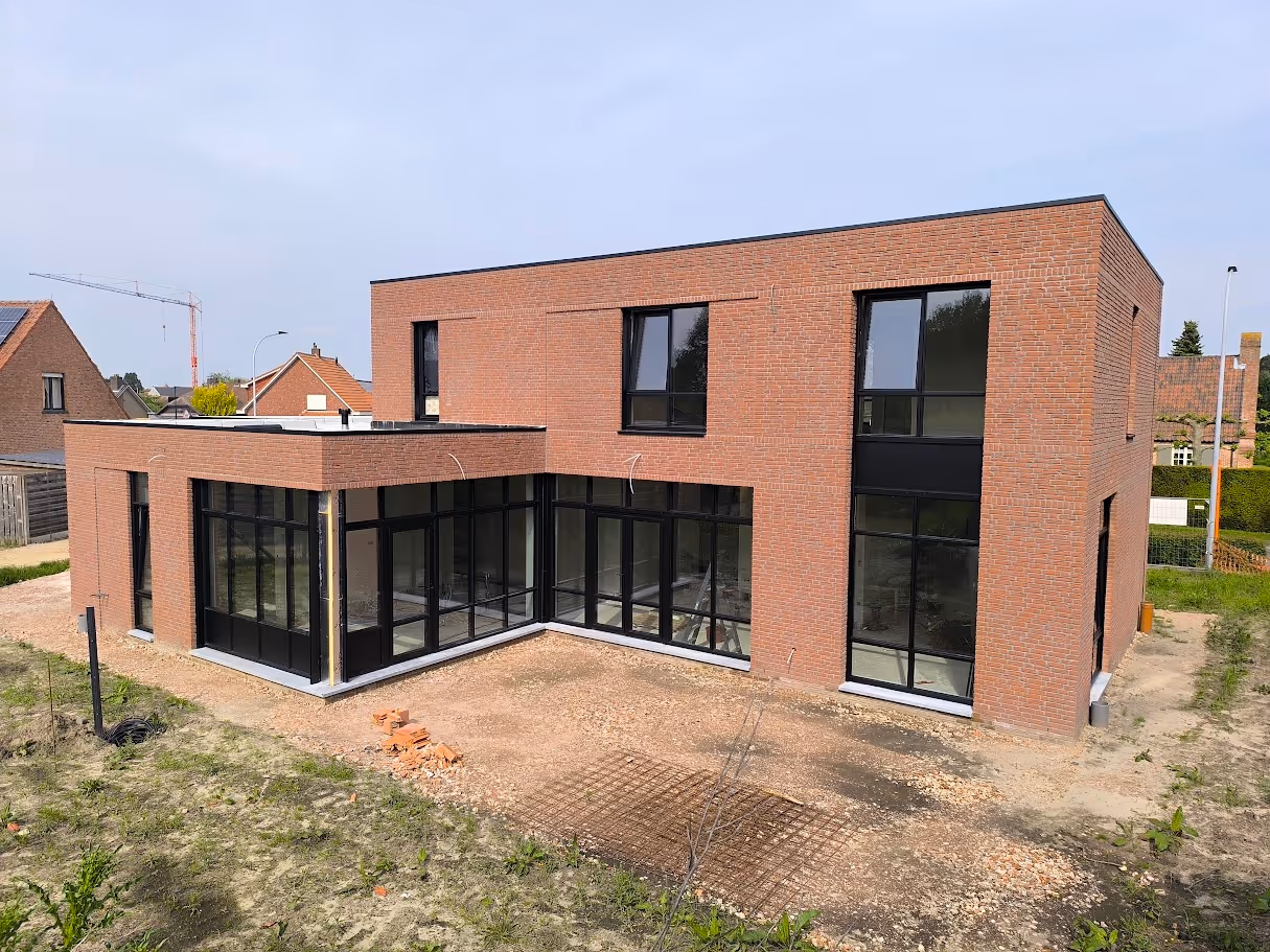 Modern two-story brick house with large black-framed windows under a clear sky.