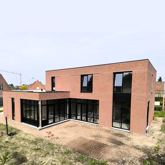 Moderne kubuswoning in ruwbouwfase met rode bakstenen gevel en zwart aluminium schrijnwerk in Poppel