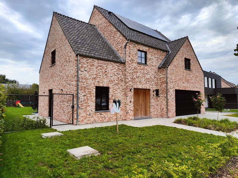 Moderne villa met dubbele puntgevel, bakstenen gevel, zonnepanelen en zwarte garagedeur te Vosselaar