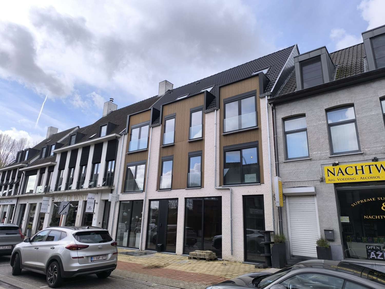 Moderne nieuwbouw met houten geveldetail en lichte gevelsteen langs een dorpsstraat in Schilde