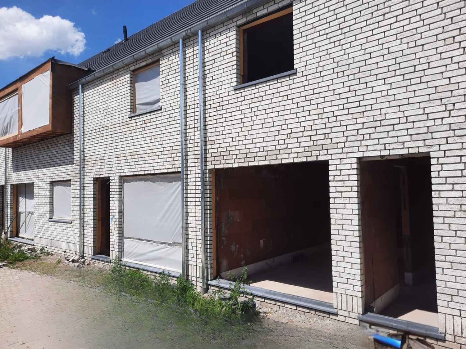 Gegroepeerde nieuwbouwwoningen in witte gevelsteen met plat dak in ruwbouwfase te Assenede