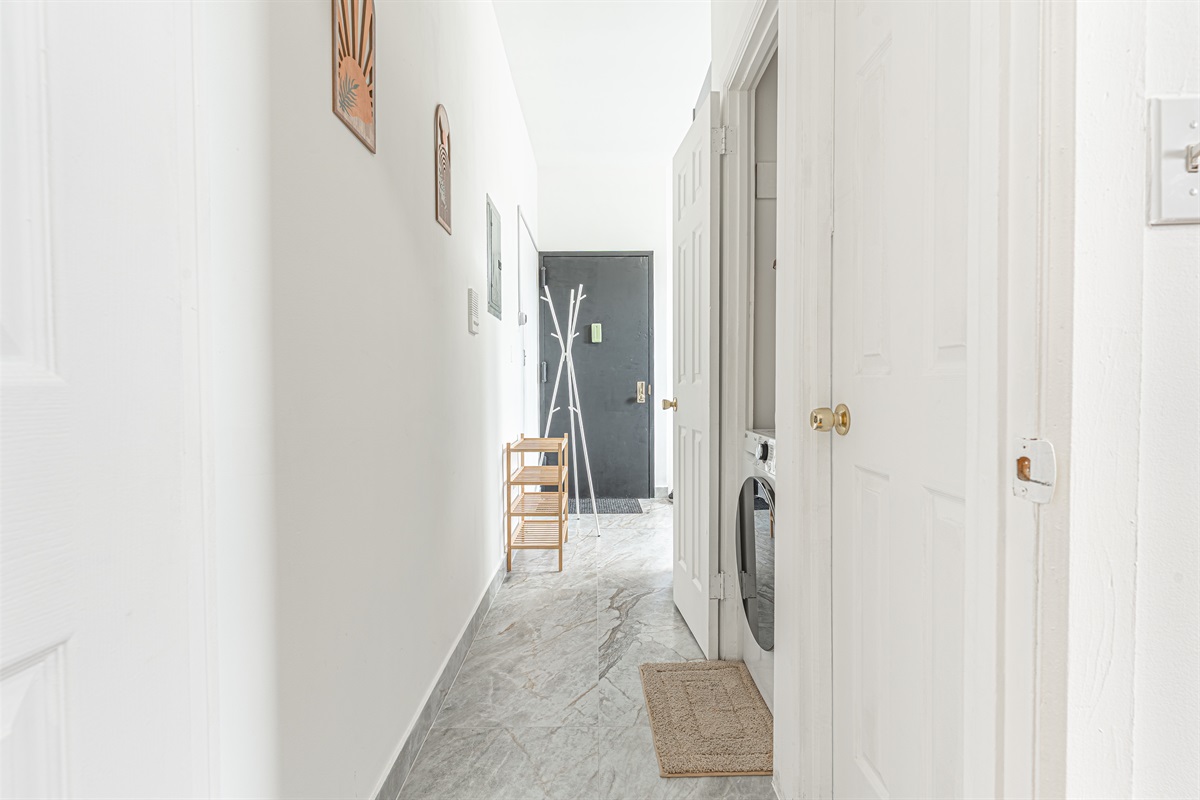 Bright, airy hallway with marble floors leading to the in-unit laundry closet — fresh and well-kept throughout.