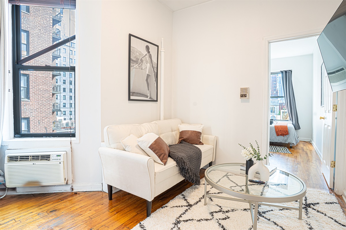 Bright living area with AC, cozy sofa, and view into the bedroom