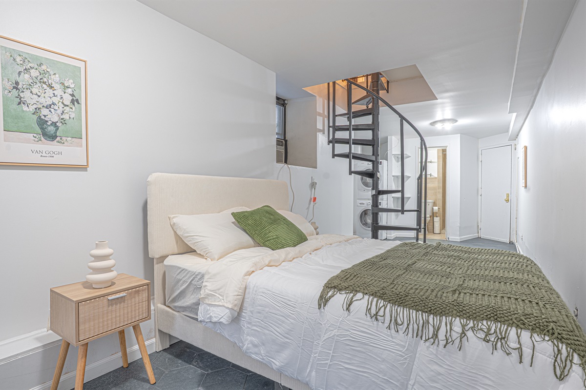 Second bedroom with a cozy bed and a charming spiral staircase — characterful multi-level living on the Upper East Side.