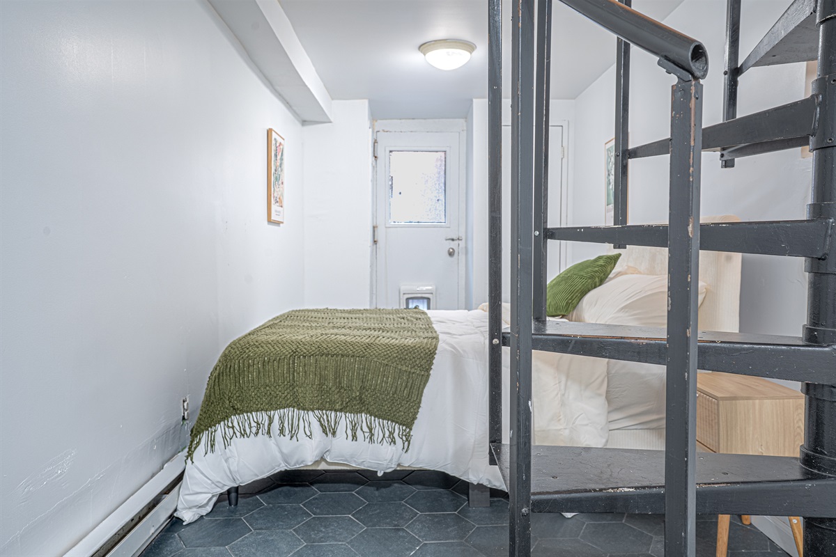 Tucked-away second bedroom with hex-tile floor and spiral stair access — a private, characterful space to recharge.