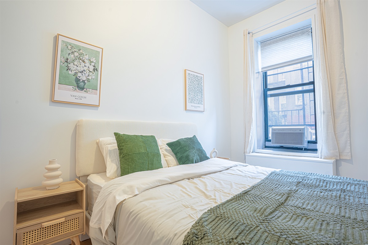Bright bedroom with an upholstered headboard, big sunny window, and air conditioning — comfortable rest year-round.