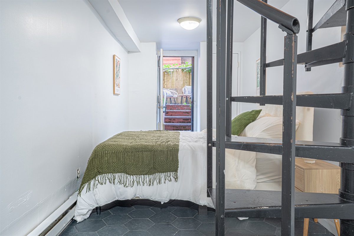 Garden-level second bedroom by the spiral stair, steps from the backyard — quiet, private, and full of character.