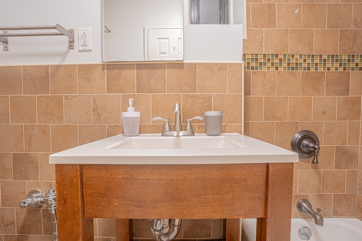 Bathroom vanity with a stylish sink, mosaic tile accent, and tub — a comfortable space to freshen up.