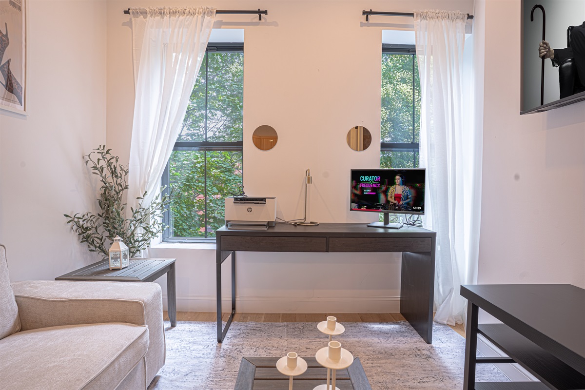 Cozy room with sofa, desk, printer, and natural light—perfect for work or relaxing
