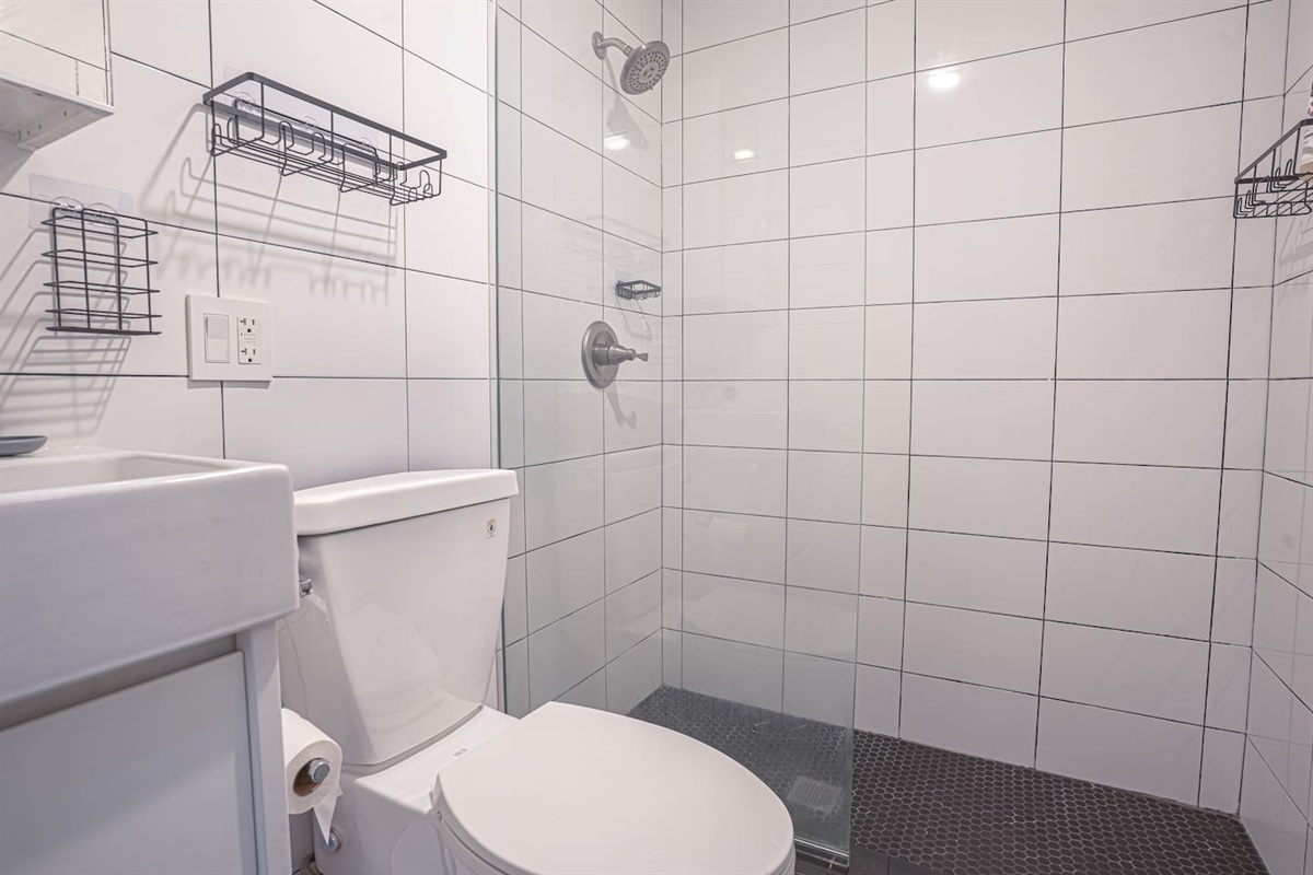 Modern bathroom with sleek white tile walls, glass walk-in shower, and updated fixtures. Thoughtfully designed with a cl