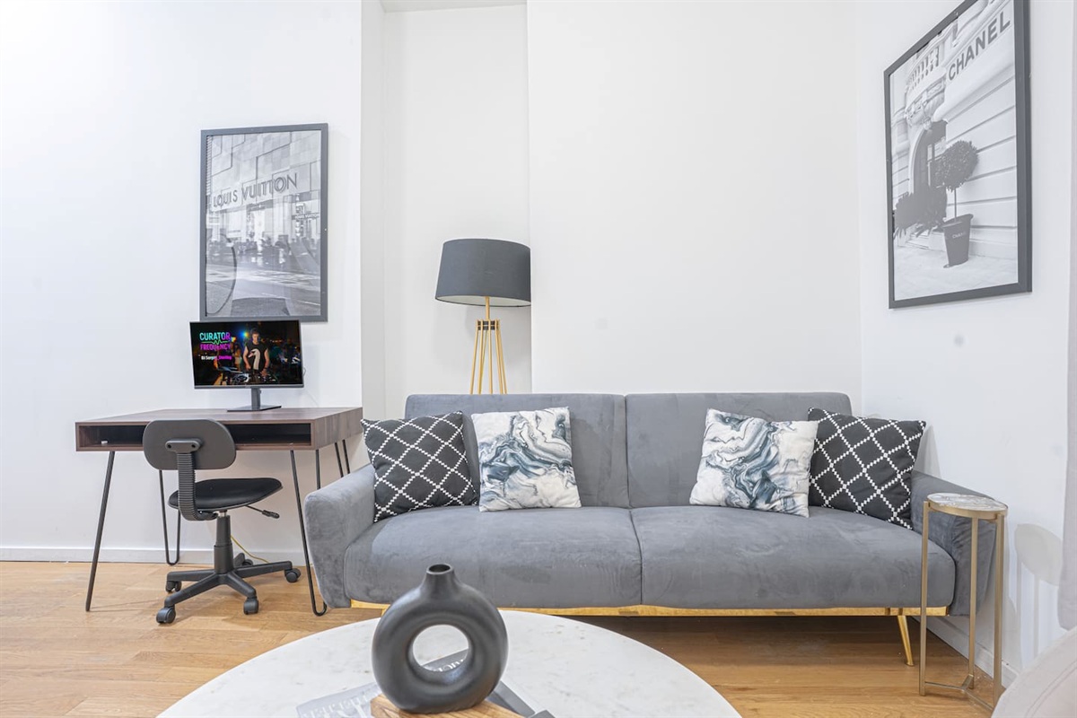 Living area with a plush gray futon accented with pillows, complemented by chic artwork and a modern floor lamp. A dedic