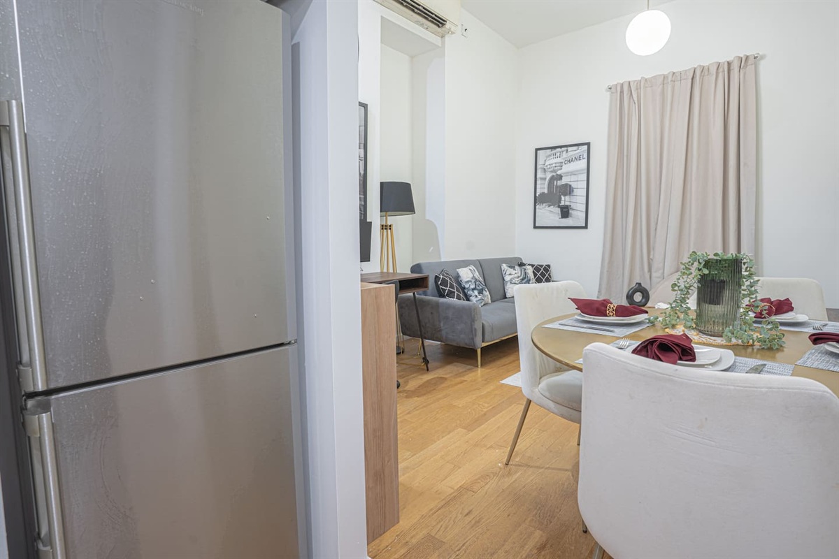 Bright and inviting open-plan layout with stainless steel refrigerator, cozy dining area set for four, and a comfortable