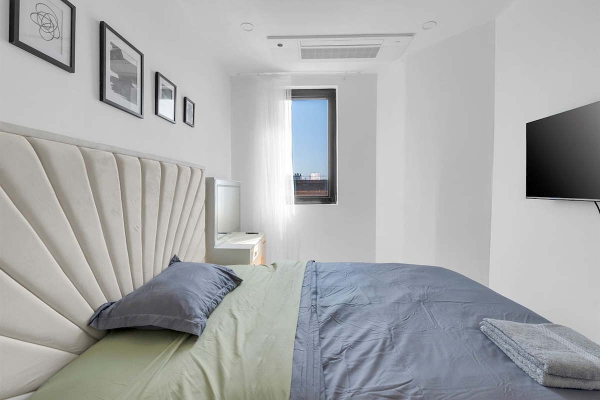 Inviting bedroom with a tufted headboard, framed art and a wall-mounted TV — cozy and stylish.