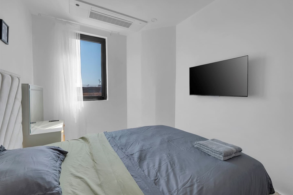 Sunlit bedroom with fresh linens, plush towels and a smart TV — comfortable, easy rest.