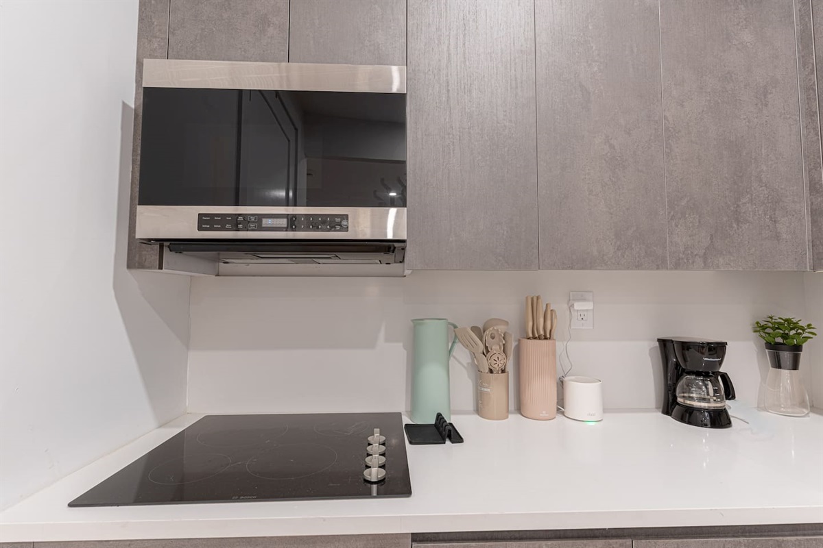 Full kitchen with cooktop, range hood and coffee station on bright quartz counters — start your morning before catching