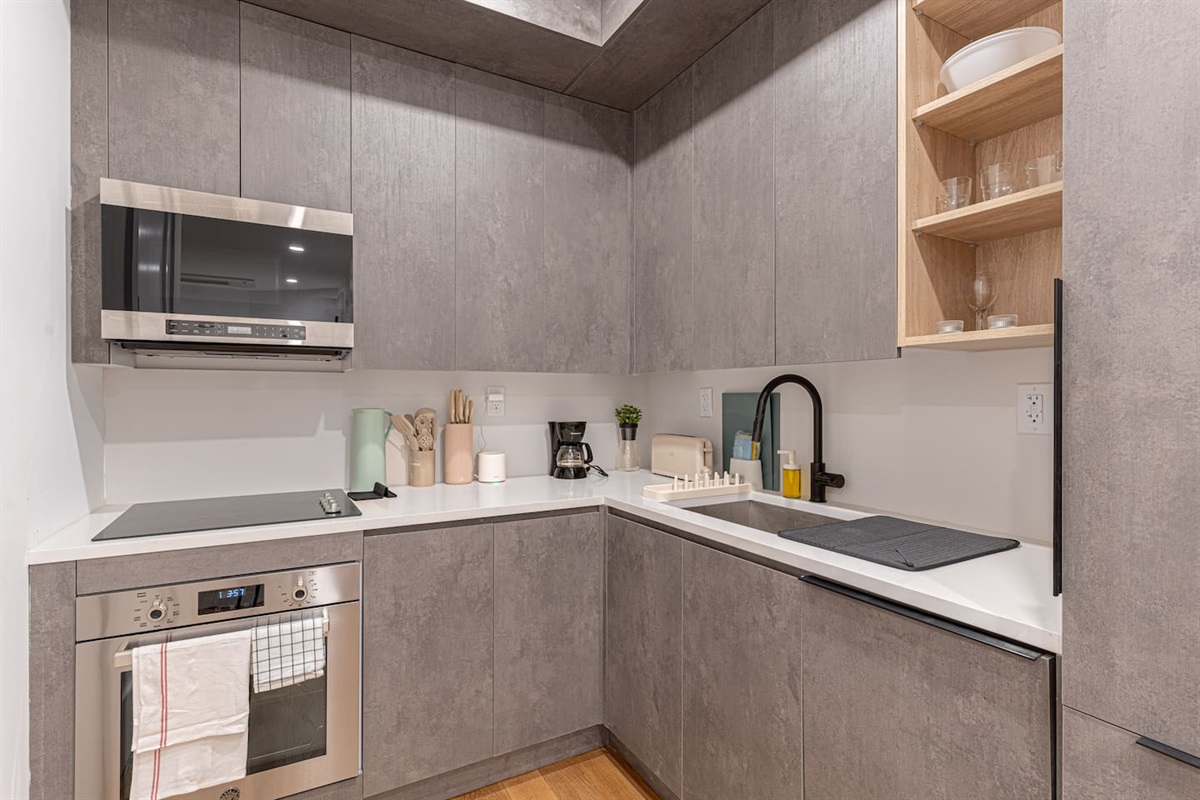 Fully equipped kitchen with stainless microwave, cooktop, sleek cabinetry and quartz counters — cook in and save while y