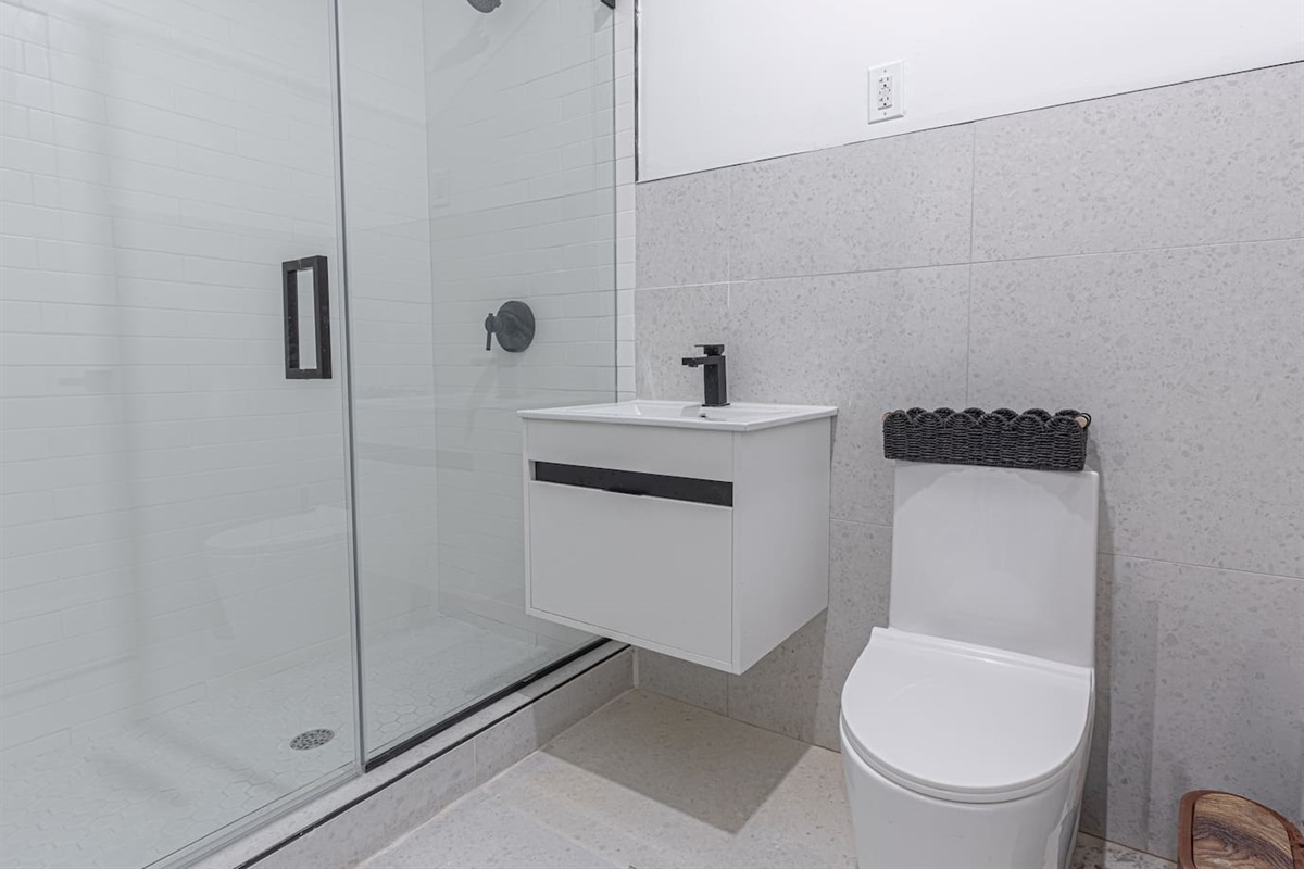 Bright, contemporary bathroom showcasing a white vanity, matching toilet, and a glass-enclosed shower with sleek black h