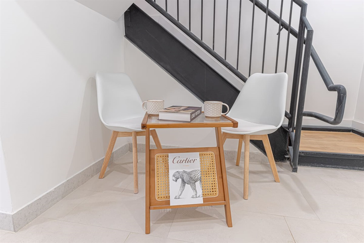 A cozy nook featuring two white chairs and a small wooden table tucked under a black staircase.