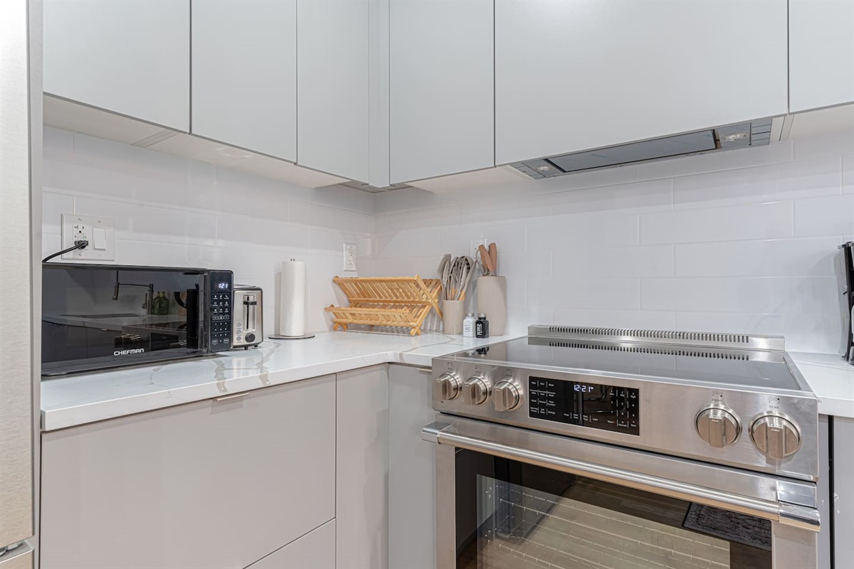 Sleek, fully stocked kitchen with stainless range, microwave, toaster, and plenty of prep space. Clean stone counters, w