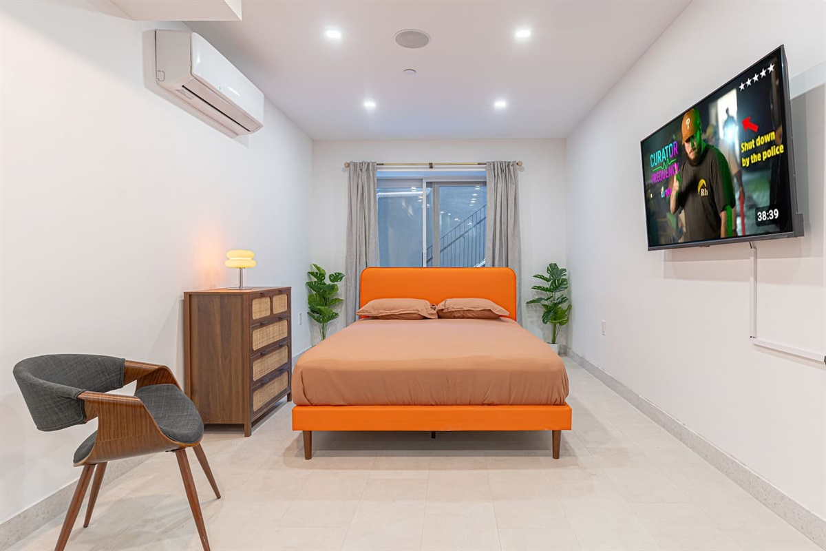 Bright, spacious bedroom with a bold orange statement bed, smart TV, and A/C for year-round comfort. Clean modern design