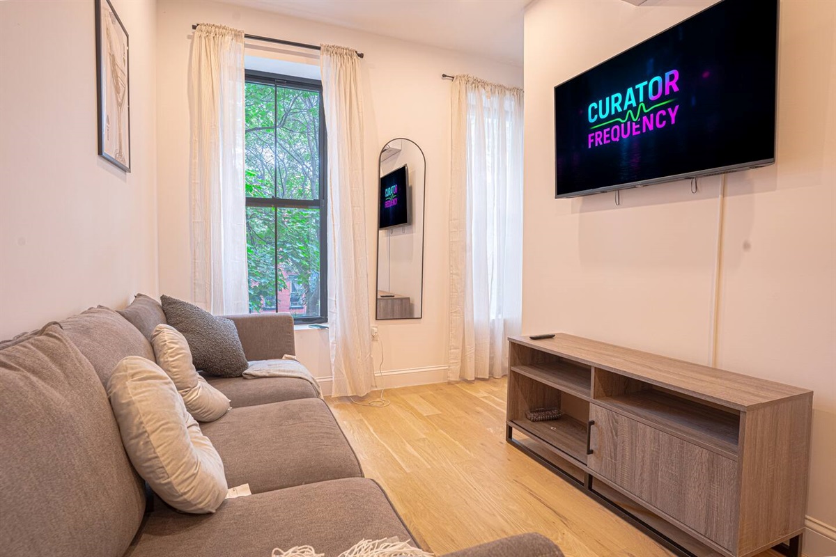 Bright living room with sofa, smart TV, large windows and stylish artwork for relaxation.