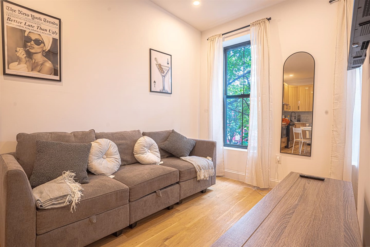 Cozy sunlit living room with comfy sectional sofa, art-lined walls and lush window views.