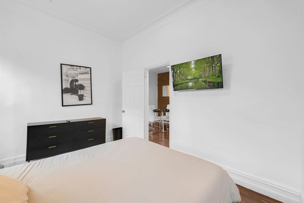 Restful bedroom with a comfortable bed, dresser, and wall-mounted smart TV — quiet nights in one of Brooklyn's most belo