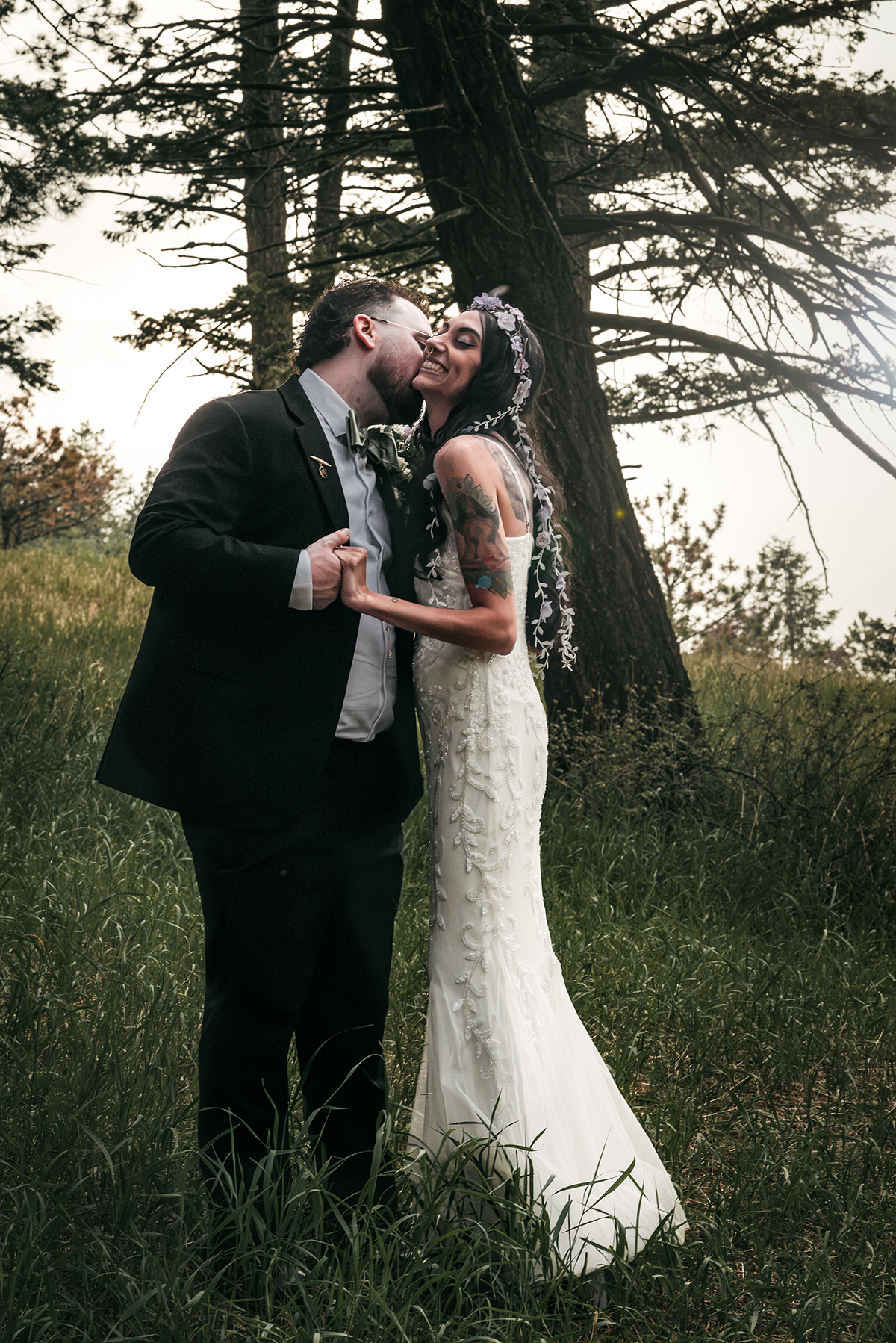 A groom whispering into his bride's ear and kissing her neck amongst Pine trees in Colorado.
