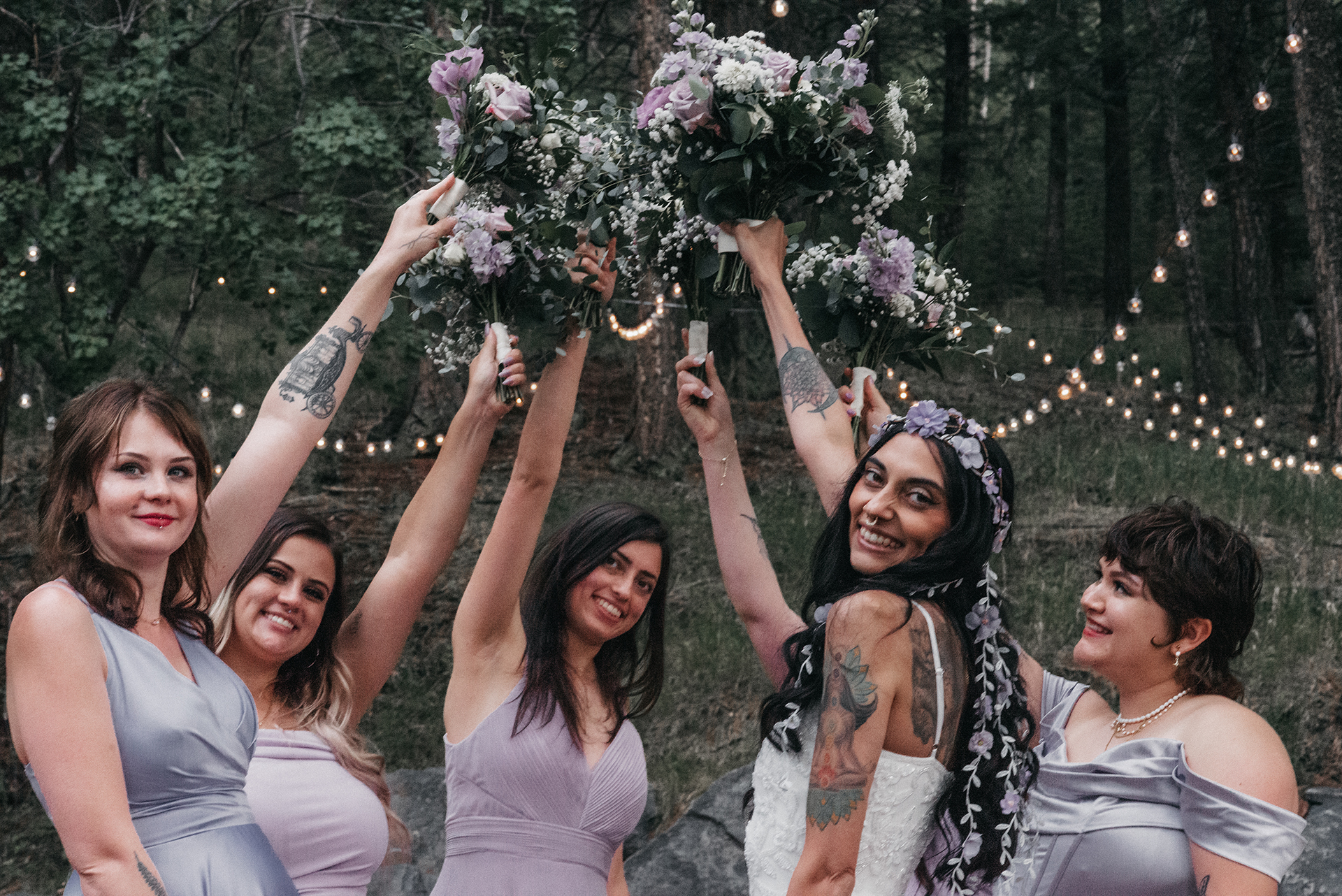 A Bridal group of women in lavender dresses  raising their bouquets up to the sky.