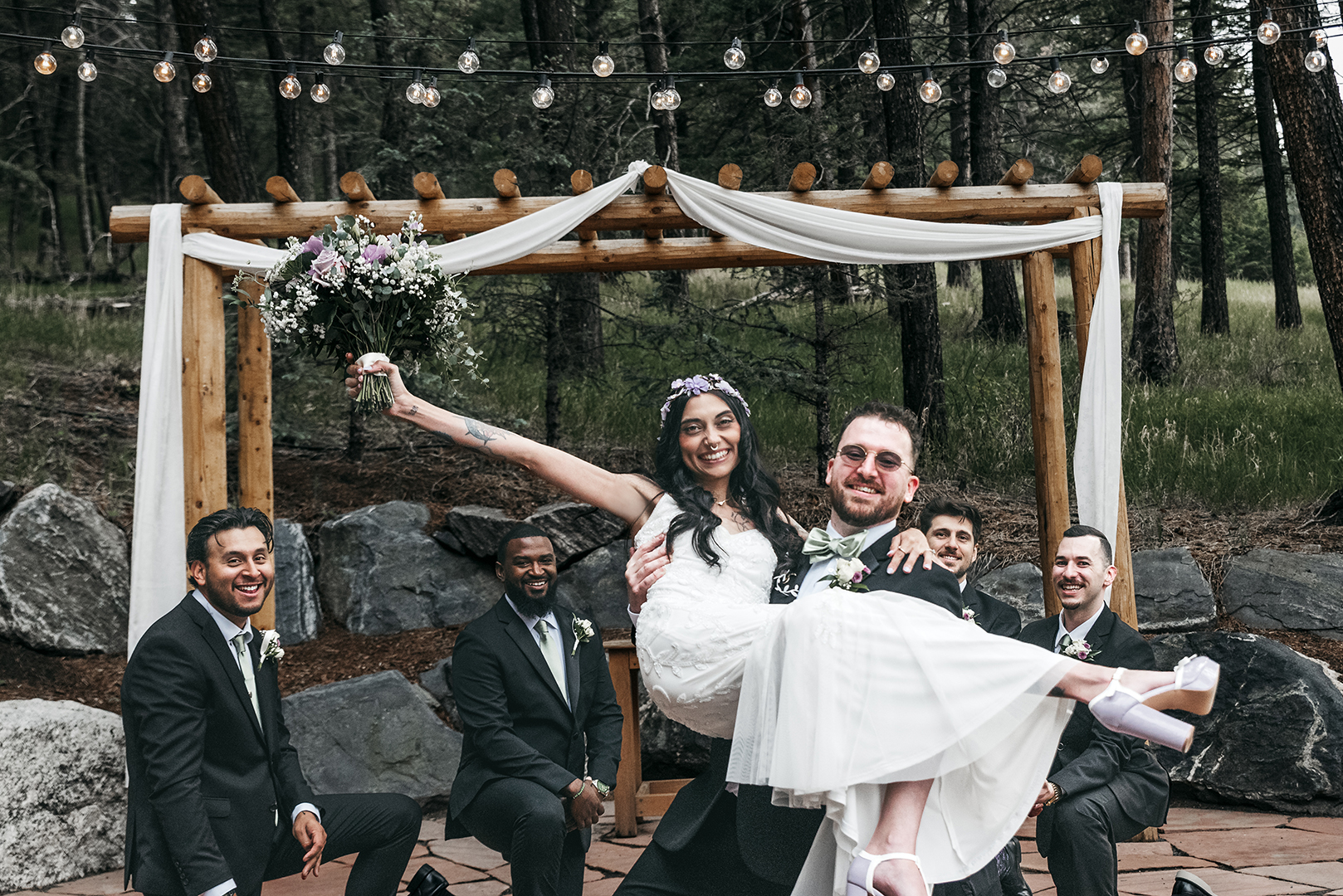 A groom lifting his wife in a pose after their wedding vows, with his groomsmen taking a knee behind them.  