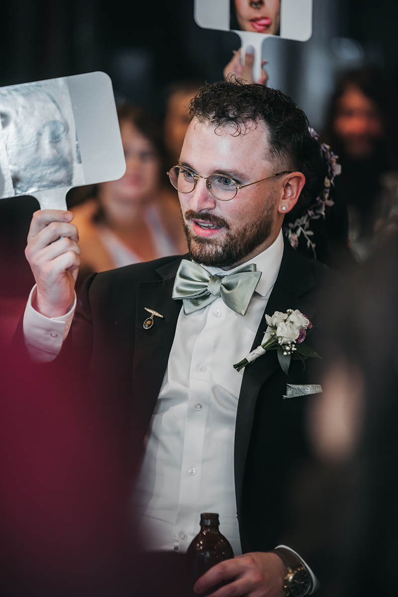 A smiling groom/ husband playing a wedding game with his wife at his backside. 