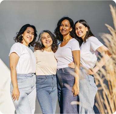 Diverse group of four smiling women in casual wear standing closely together outdoors.