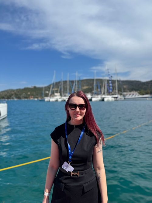 Team member of High Tide standing on the dock with yachts in blue water behind her.