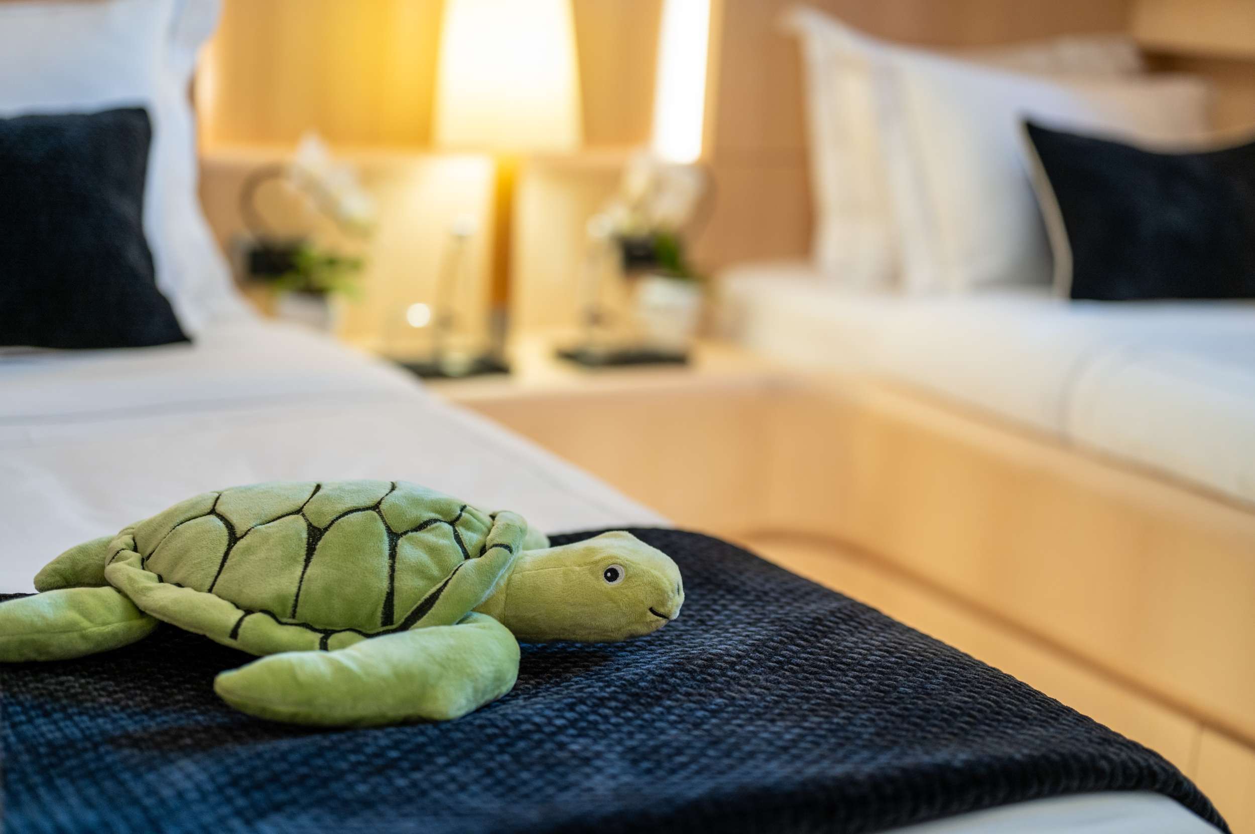 Plush turtle toy placed on a neatly made yacht bed with soft lighting and elegant decoration in the background.