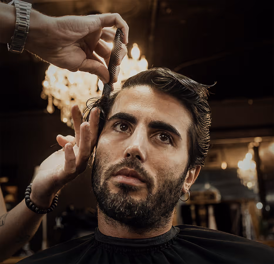 Man receiving a classic haircut, with a barber combing his wet hair in a stylish barbershop.