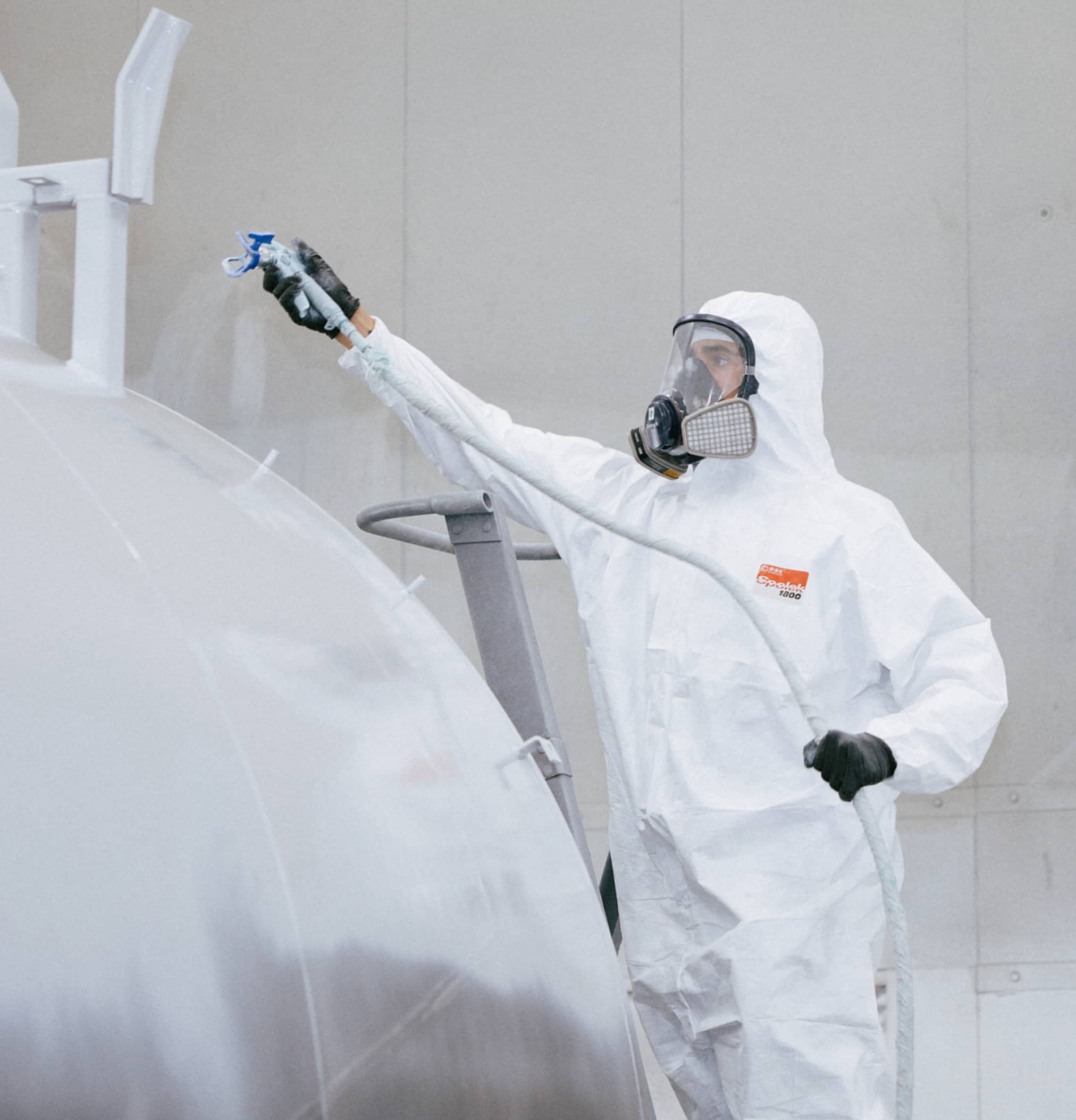 Employee in PPE spraying a large cylinder with paint