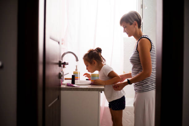 Mom helping young daughter brush teeth Mom helping young daughter brush teeth Parent helping child rinse with a small cup of warm water in a bright bathroom setting stock pictures, royalty-free photos & images