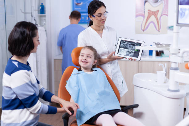 Dentist discussing diagnosis with child parent Dentist discussing diagnosis with child parent holding tablet pc with radiography. Stomatologist explaining teeth diagnosis to mother of child in health clinic holding x-ray. Smiling child sitting in a dental chair, dentist showing her teeth on a monitor. stock pictures, royalty-free photos & images