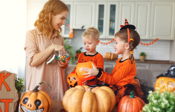 happy Halloween! mother treats children with candy at home happy Halloween! a mother treats children with candy at home  Parent and two kids sorting Halloween candy on a kitchen counter, laughing together stock pictures, royalty-free photos & images