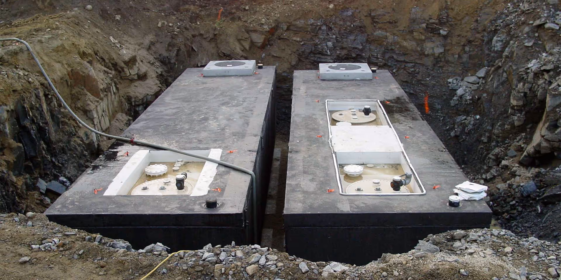 Two large rectangular underground storage tanks installed in a dug-out construction site, surrounded by dirt and rocks.