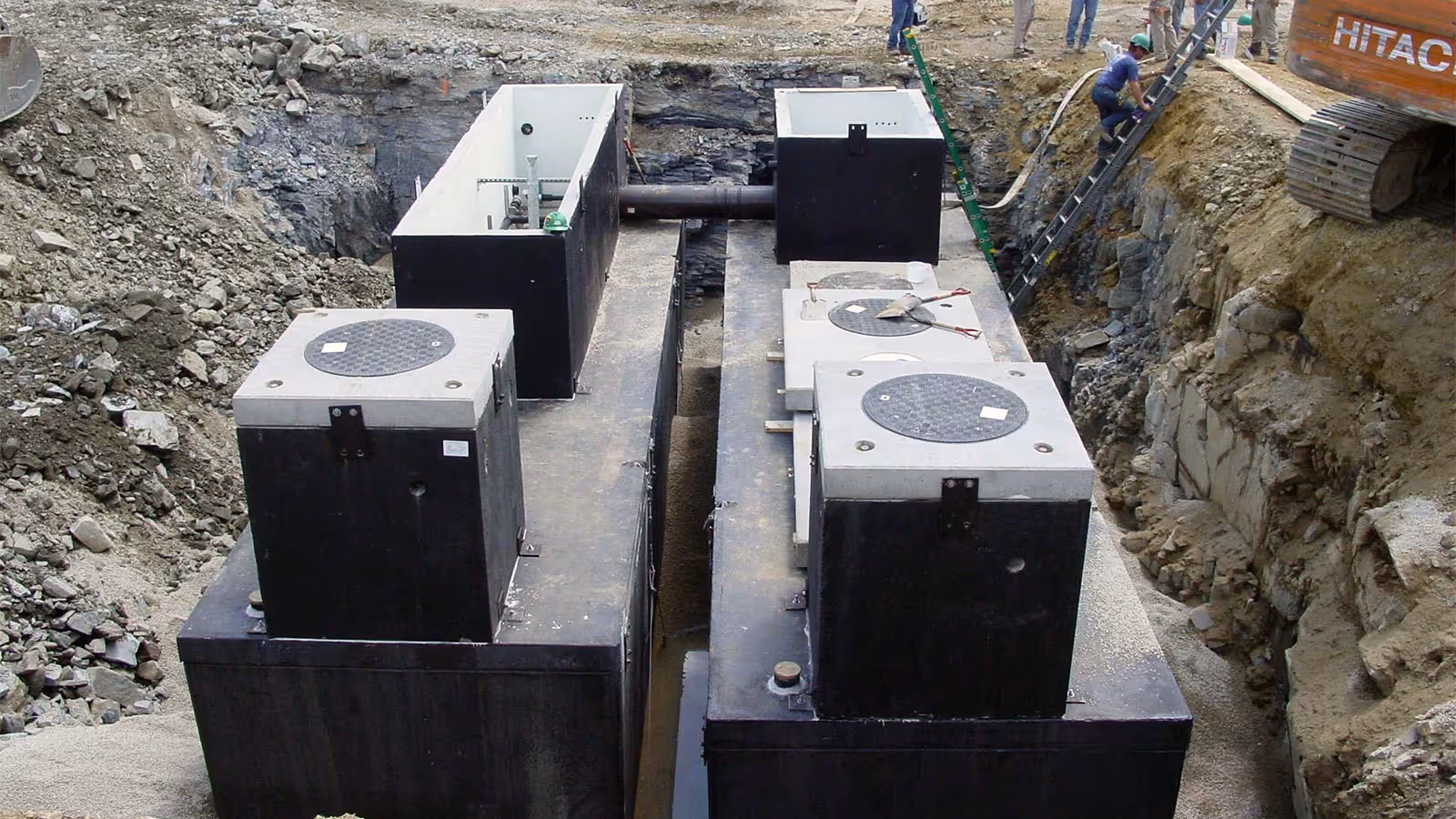 Large underground water tanks being installed in a construction site with workers and machinery visible in the background.