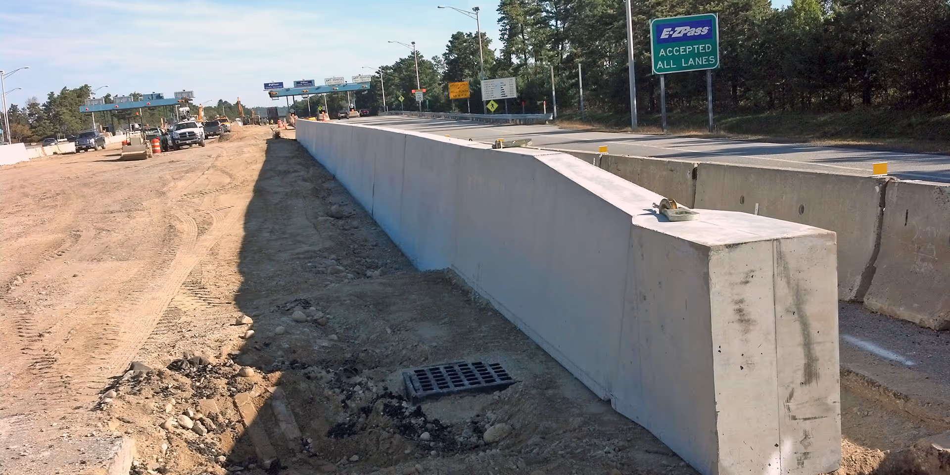 Concrete barriers line a highway under construction with EZPass and other road signs visible in the background.