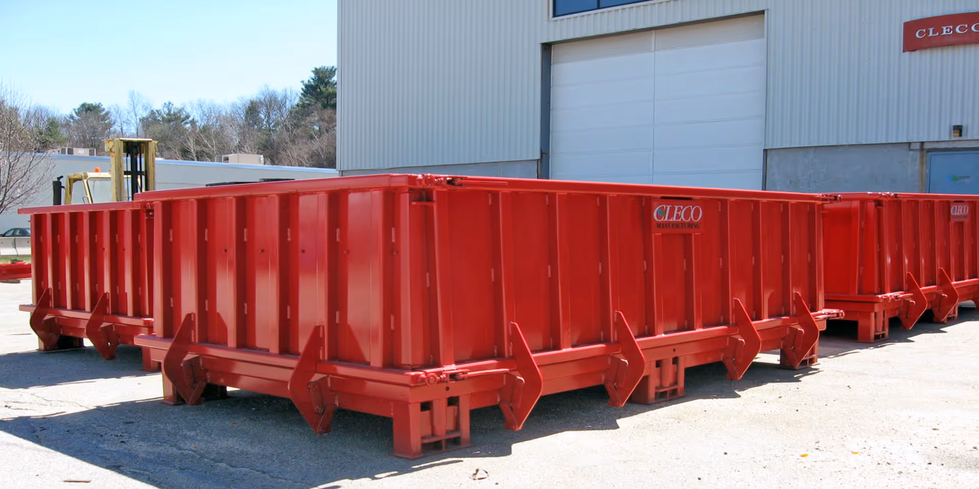 Large red industrial dumpsters are lined up outside a building with a closed garage door.