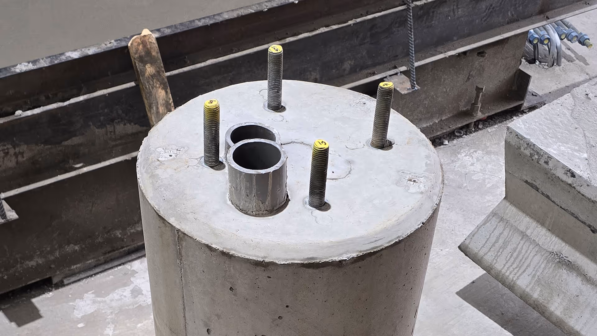 A round concrete base with four exposed anchor bolts and three metal pipes protruding from the center.