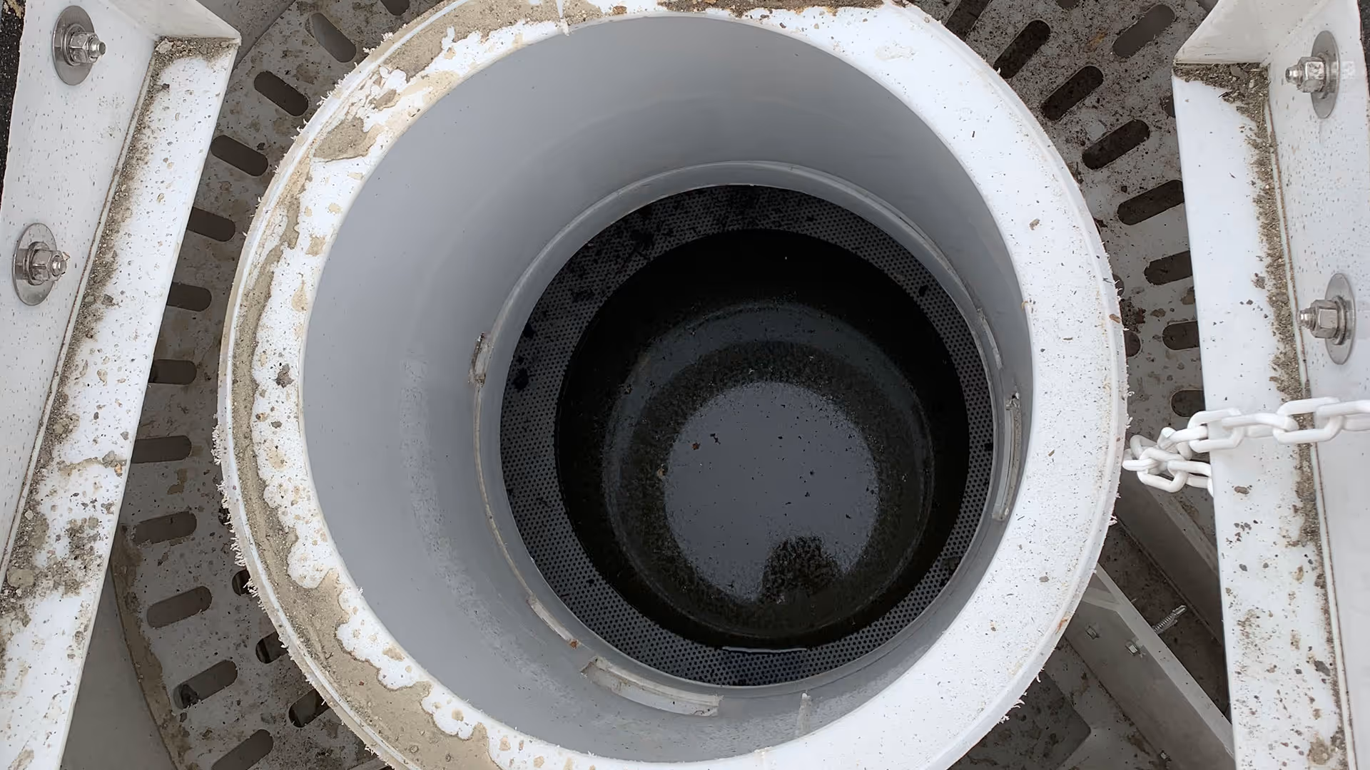 Top view of a large, white industrial tank with a circular opening, containing some dark liquid at the bottom.